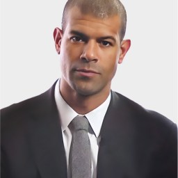 A man in a black suit and gray tie is facing forward against a plain white background.