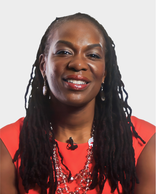 A woman with long braided hair, wearing a red top, earrings, and a beaded necklace, is smiling at the camera against a plain white background.