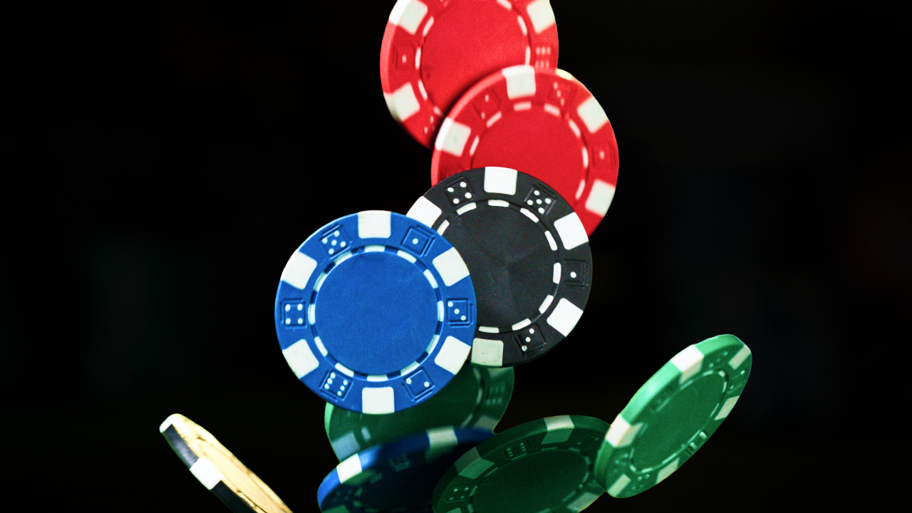 A group of colorful poker chips, including red, blue, black, and green, fall through the air against a black background.