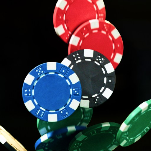 A group of colorful poker chips, including red, blue, black, and green, fall through the air against a black background.