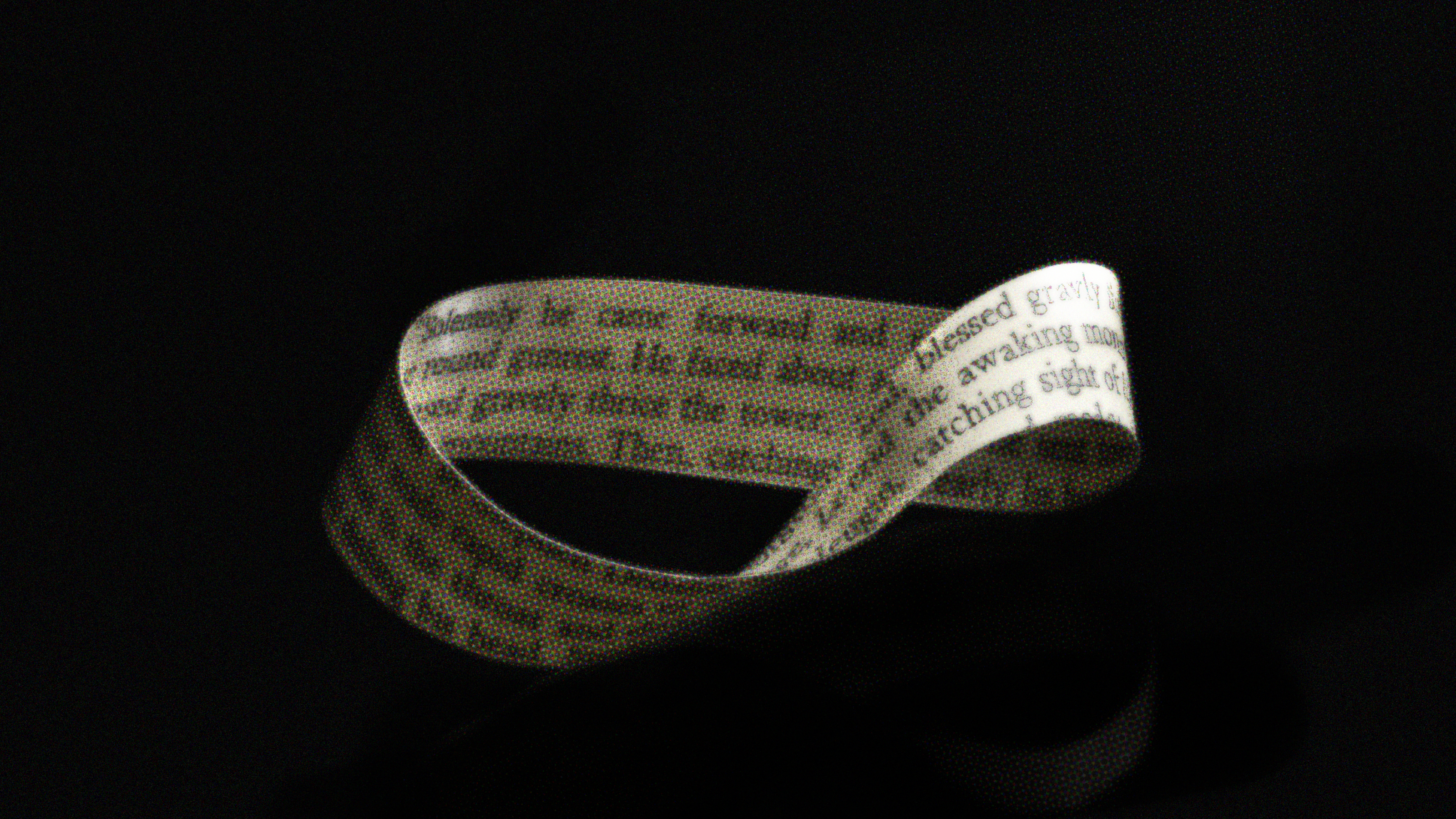 A Möbius strip made from paper with printed text is displayed against a dark background.