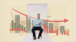 A man sits on a stool in front of a backdrop displaying a declining graph with bar charts and red trend lines, suggesting a downward trend in data.
