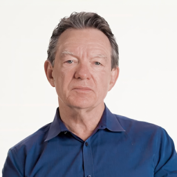 A middle-aged man with short gray hair wearing a blue button-up shirt, looking directly at the camera against a plain white background.