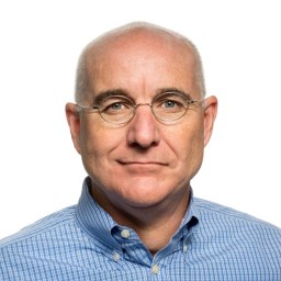 A middle-aged man with glasses, light skin, and a bald head, wearing a blue checkered shirt, facing forward against a white background.