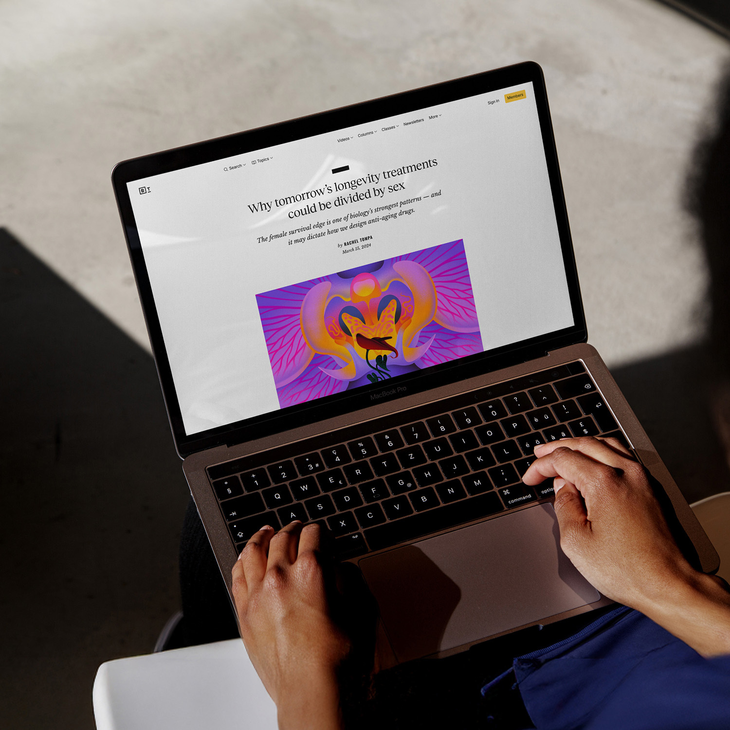 Person using a laptop, reading an article titled "Why tomorrow’s longevity treatments could be divided by sex," with an illustrated graphic displayed on the screen.