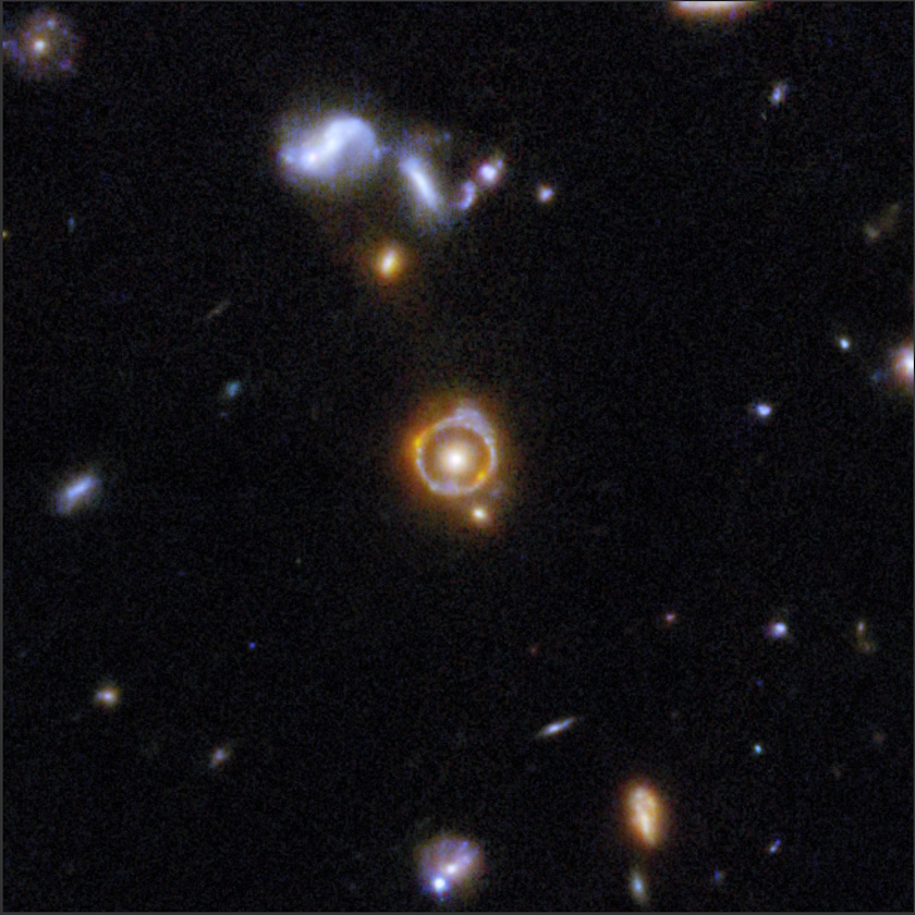 A group of galaxies in deep space, imaged by COSMOS-Web JWST, displays a prominent orange glowing ring&mdash;likely a gravitational lens&mdash;around a central object, surrounded by numerous faint stars and galaxies on a dark background.