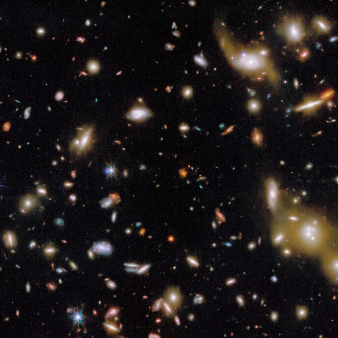 A view of deep space showing numerous galaxies of various shapes and sizes scattered across a dark background.