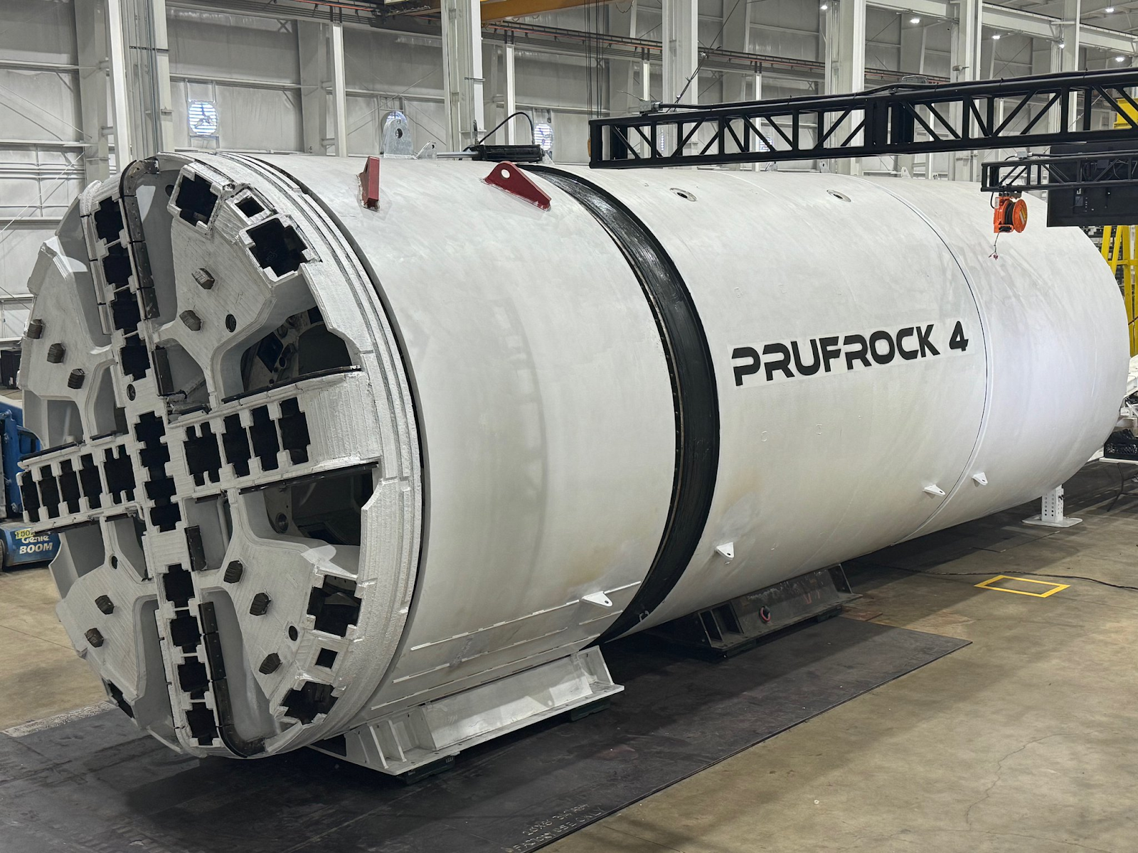 A large white tunnel boring machine labeled "PRUFROCK 4" is positioned indoors in an industrial facility.