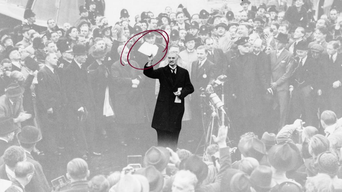A man in a dark coat holds up a signed document in front of a crowd; the document is circled in red.
