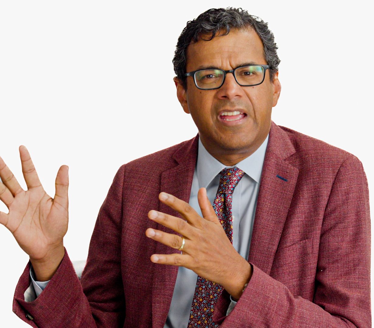 A man in a maroon suit and patterned tie gestures with his hands while speaking. The BT+ logo appears in the top right corner against a plain white background.
