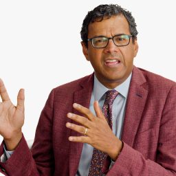 A man in a maroon suit and patterned tie gestures with his hands while speaking. The BT+ logo appears in the top right corner against a plain white background.