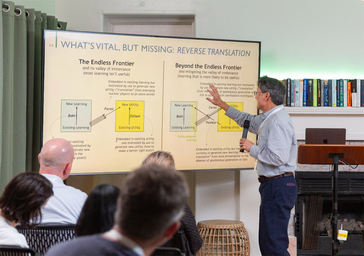 A man gives a presentation, pointing at a slide titled "WHAT'S VITAL, BUT MISSING: REVERSE TRANSLATION," which features diagrams and text explaining learning concepts.