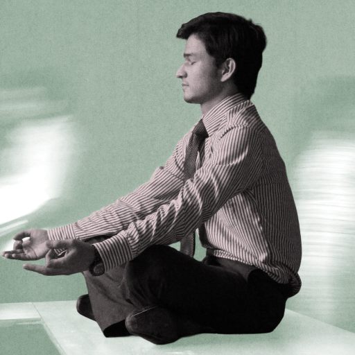 Scott Britton, in business attire, sits cross-legged on a desk meditating, while blurred figures move in the background.