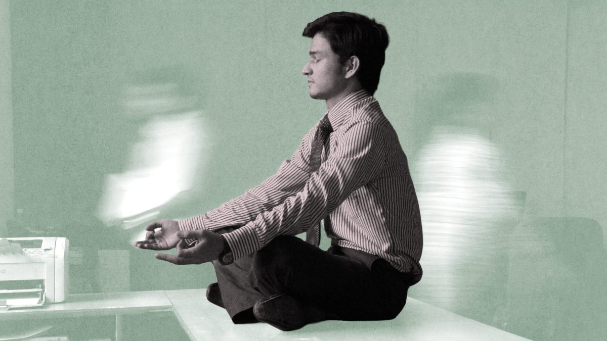 Scott Britton, in business attire, sits cross-legged on a desk meditating, while blurred figures move in the background.