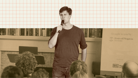 A man holding a microphone speaks to an audience in front of a bookshelf and a display with logos, including "Roots of Progress Institute" and "Big Think.