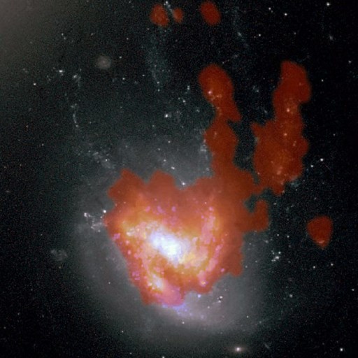 A jellyfish galaxy with a bright white and yellow core is surrounded by red clouds of gas, set against a dark background filled with stars.