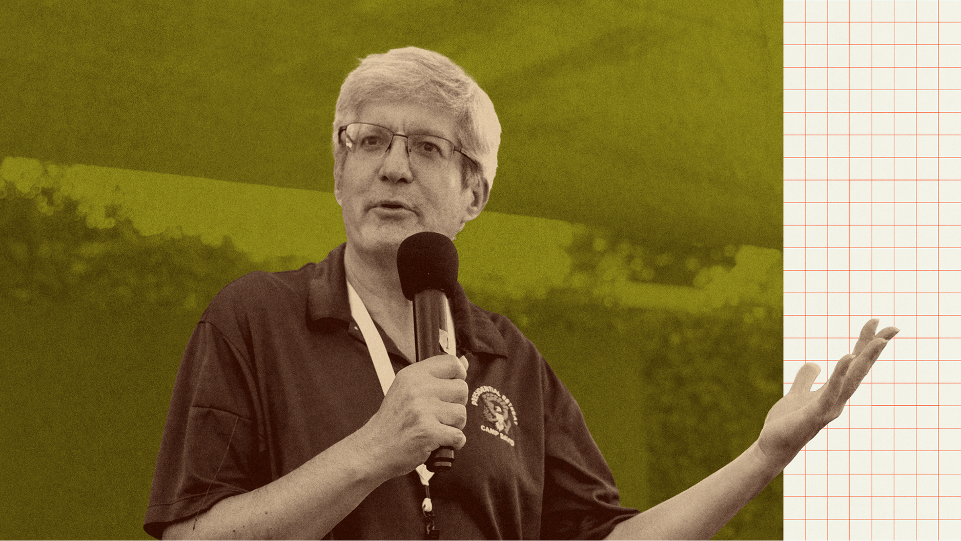 An older man with gray hair and glasses speaks into a microphone, gesturing with one hand, against a green and grid-patterned background.