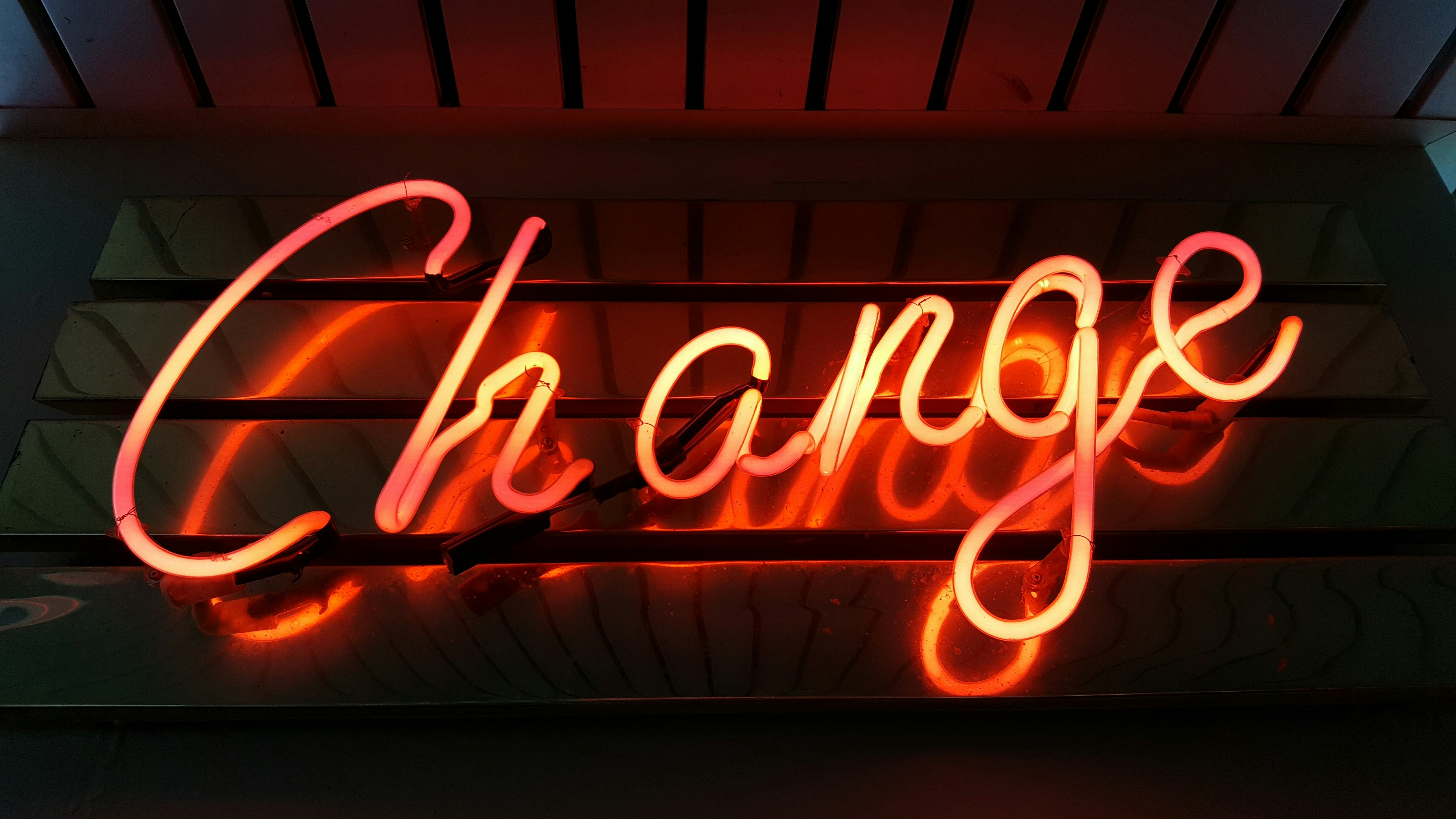 Neon sign displaying the word "Change" in cursive script, glowing in orange and red against a dark background.