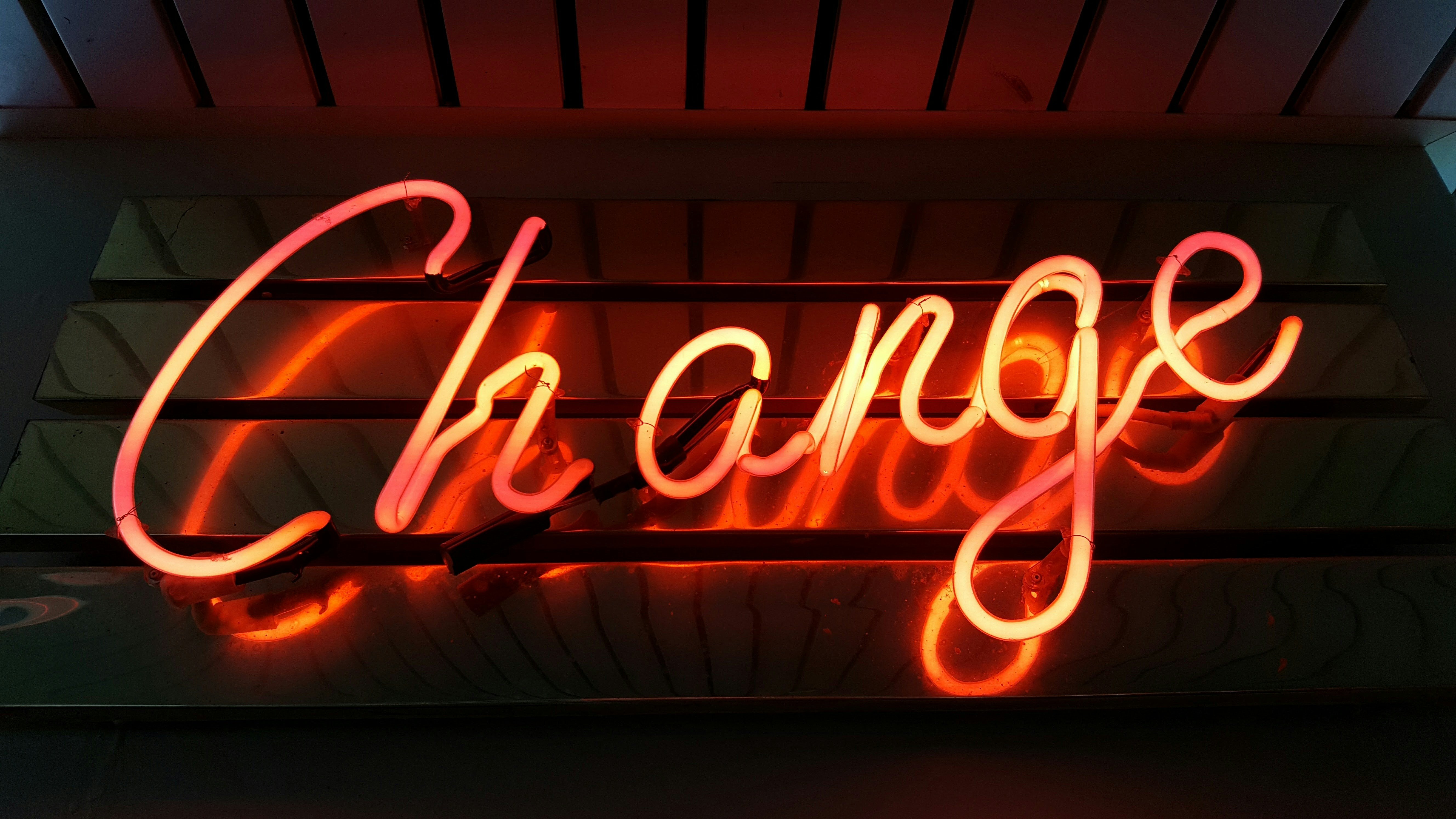 Neon sign displaying the word "Change" in cursive script, glowing in orange and red against a dark background.