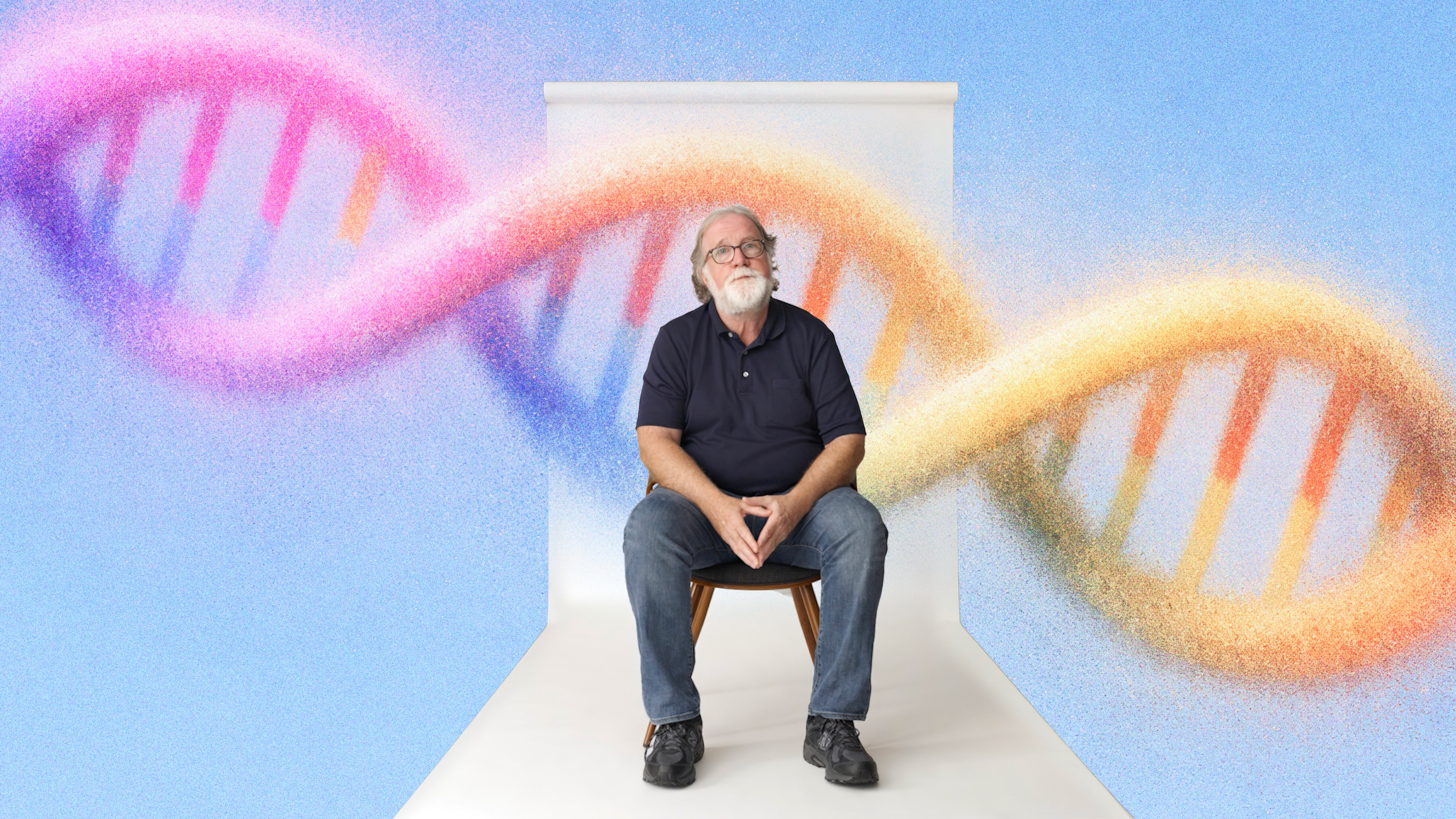 An older man with a white beard sits on a chair against a white backdrop, with a large, colorful DNA double helix illustration in the background.