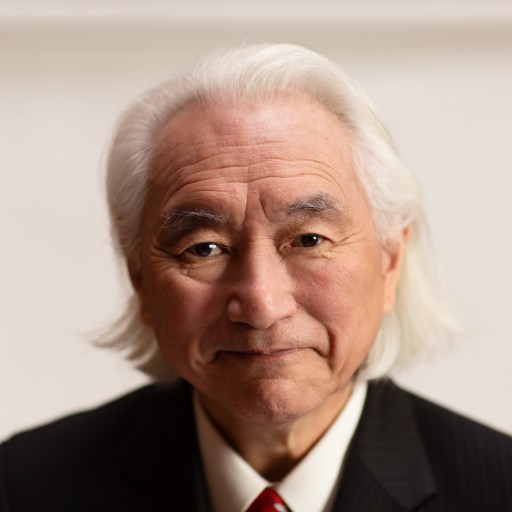 An older man with long white hair wearing a dark pinstriped suit, white shirt, and red tie, looking directly at the camera against a plain light background.