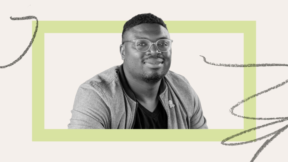 A man wearing glasses and a jacket looks at the camera, seated in front of a light background with a green rectangular frame and gray squiggle lines.
