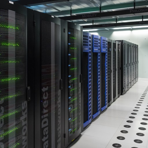 A row of black and blue server racks in a data center, where LLMs power chatbot solutions, with illuminated green lights and a white tile floor with black circular vents.