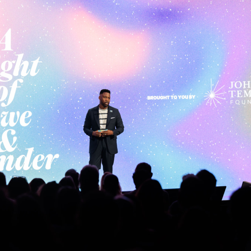 A man stands on stage before an audience, with a backdrop reading "A Night of Awe & Wonder" and the John Templeton Foundation logo.