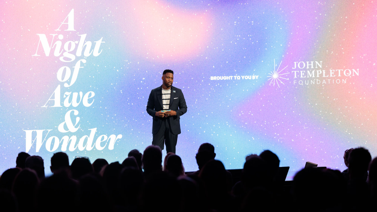 A man stands on stage before an audience, with a backdrop reading "A Night of Awe & Wonder" and the John Templeton Foundation logo.