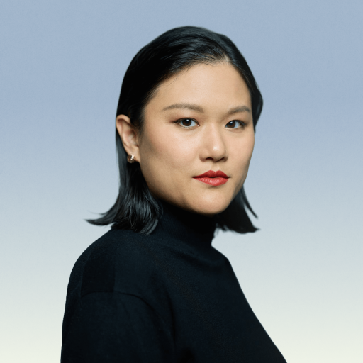 A woman with straight black hair, wearing a black turtleneck, poses against a blue-to-white gradient background.