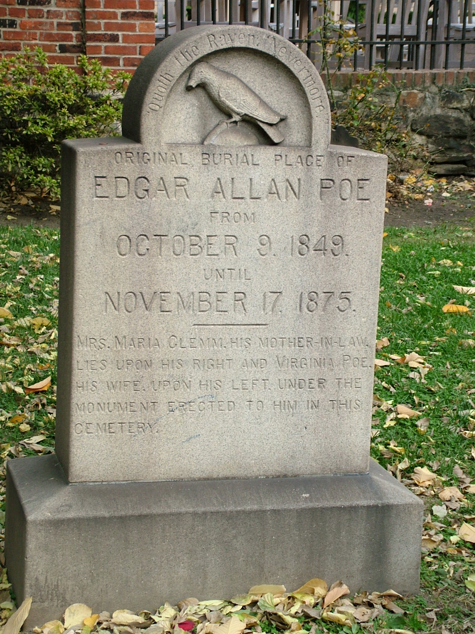 Gravestone marking the original burial place of Edgar Allan Poe, detailing his burial dates and those of his relatives, surrounded by grass and fallen leaves.