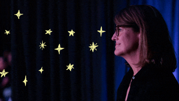 A woman with glasses stands in profile against a dark background with illustrated yellow stars scattered beside her.