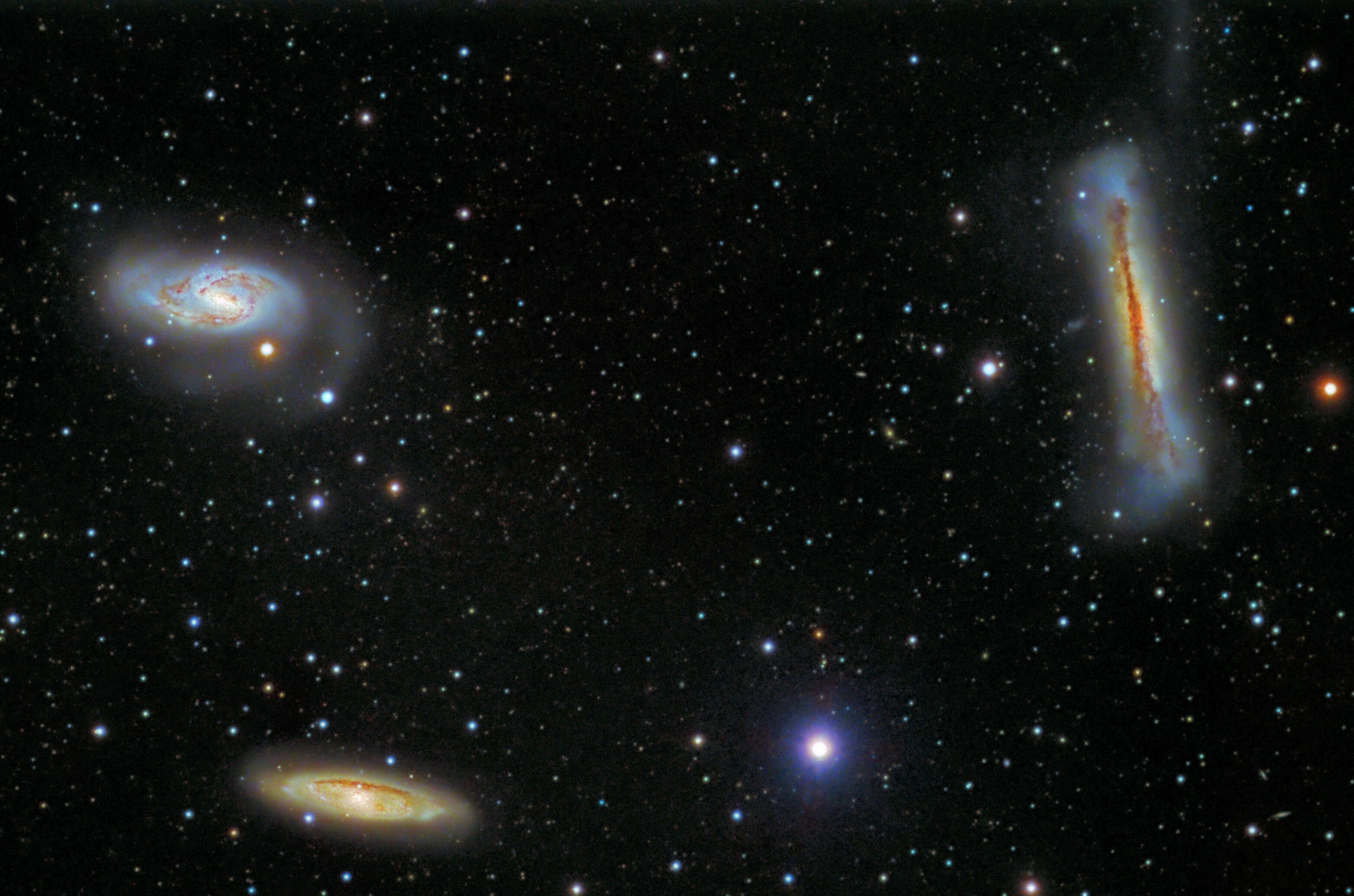 Three distinct spiral galaxies, some nearby and others far away, appear among numerous stars against a dark background in the universe.