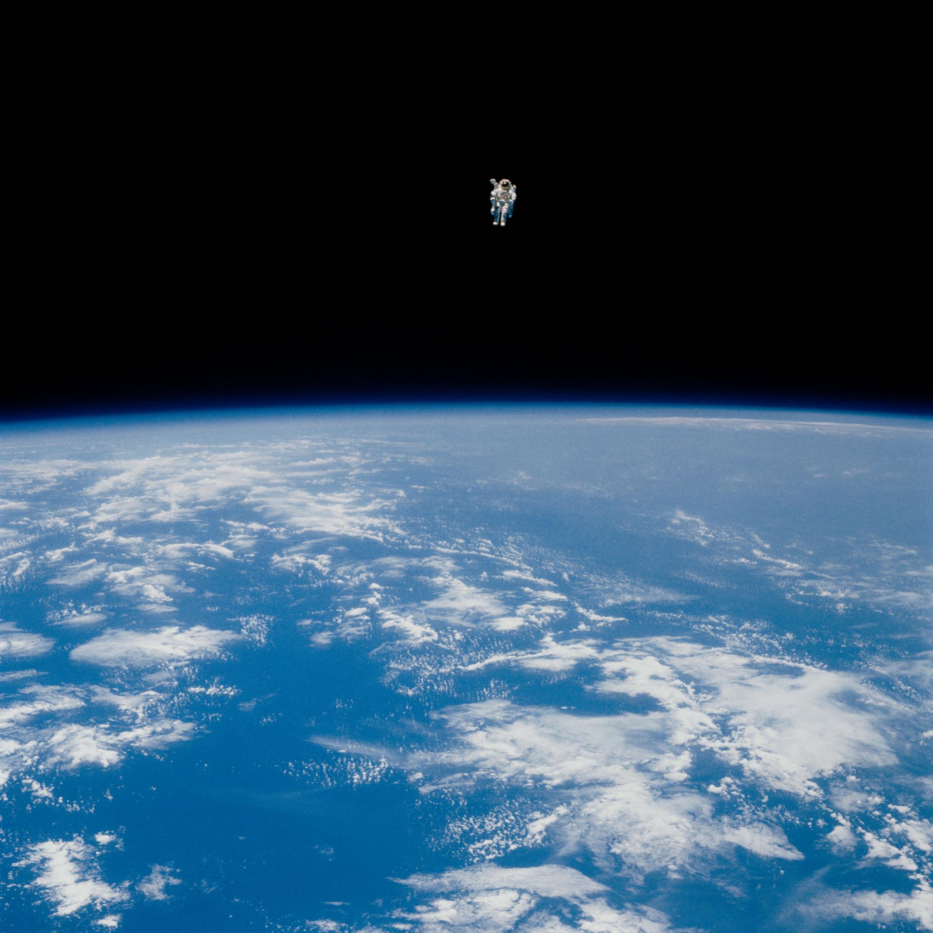 An astronaut in a spacesuit floats alone above Earth, with the planet's blue surface and clouds visible below against the blackness of space&mdash;an image capturing humanity&rsquo;s quest for discovery.