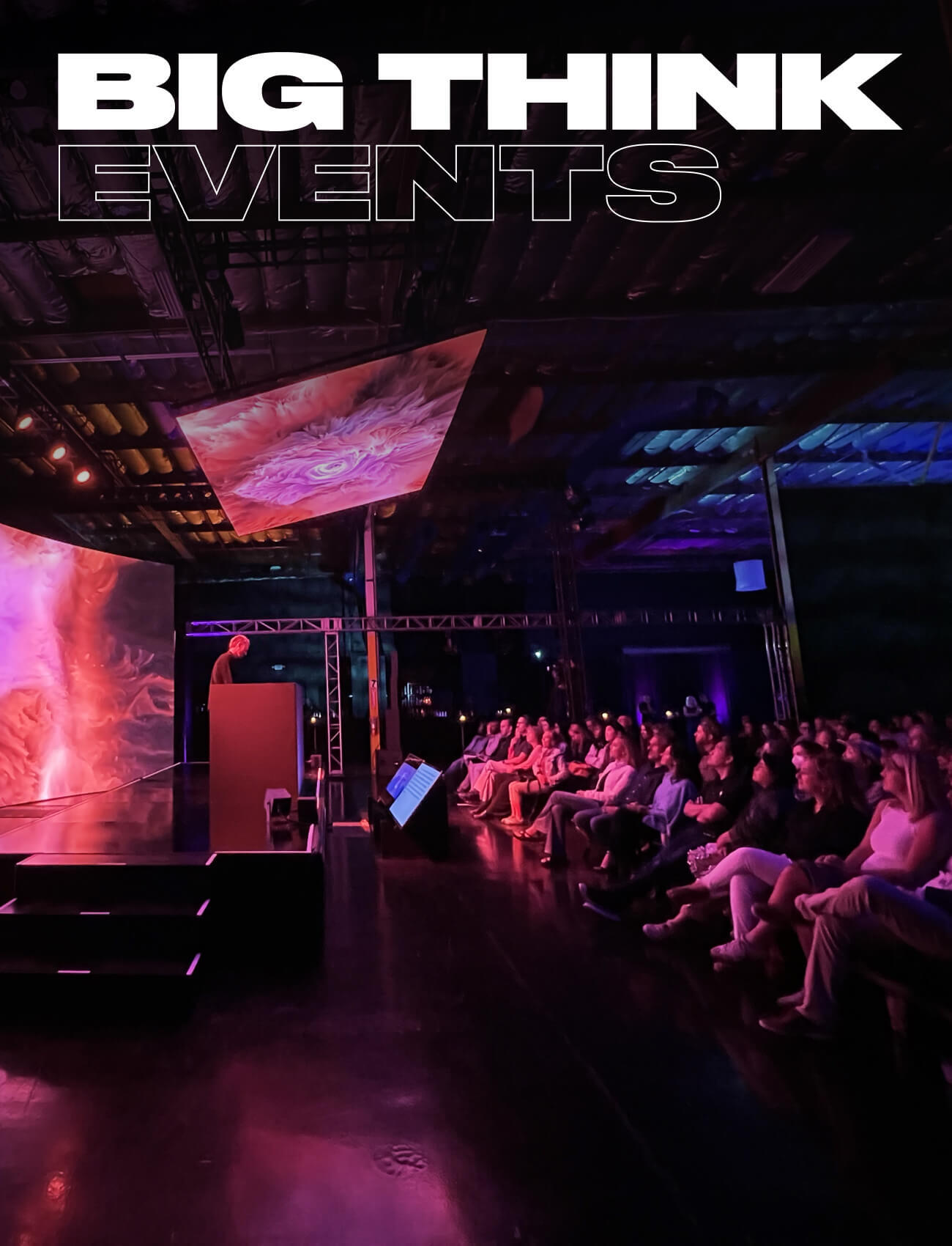 A speaker presents on stage to an audience at an event, with colorful lights and "BIG THINK EVENTS" displayed above.