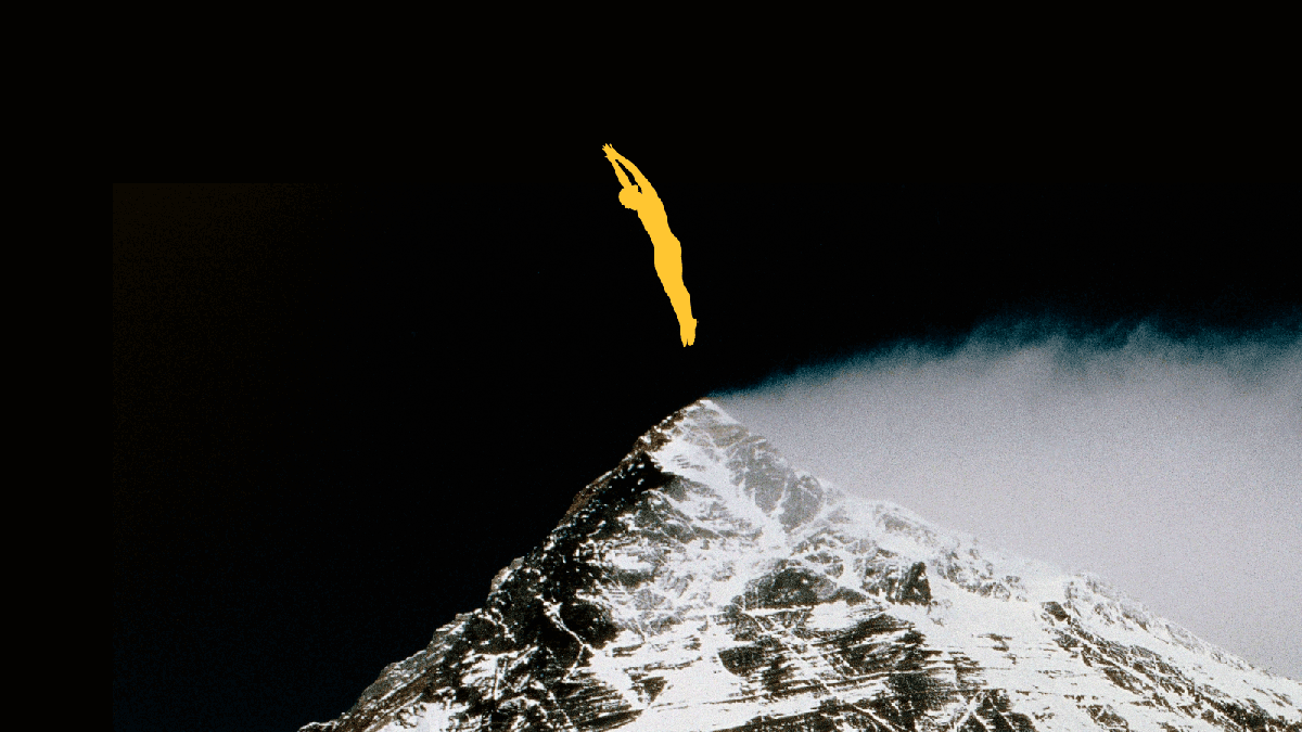 A yellow silhouette of a person dives above the snow-covered peak of a mountain against a dark sky.