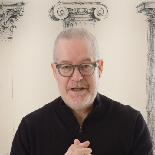 A man with glasses and a gray beard stands in front of illustrations of three classical columns, each with a different capital style.