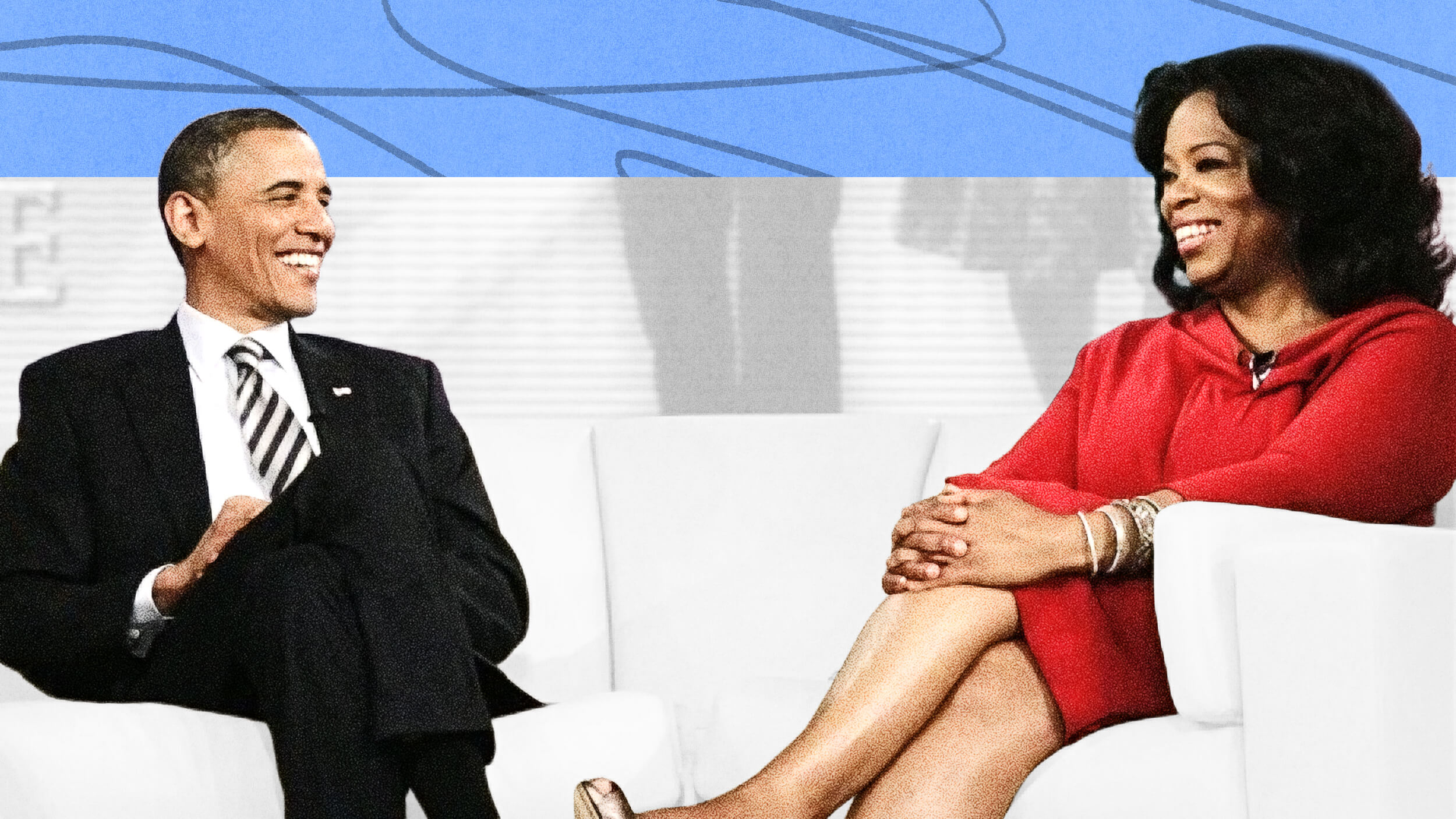 Two people sit on white chairs facing each other, both smiling and dressed formally, on a brightly lit stage with a blue and white background.