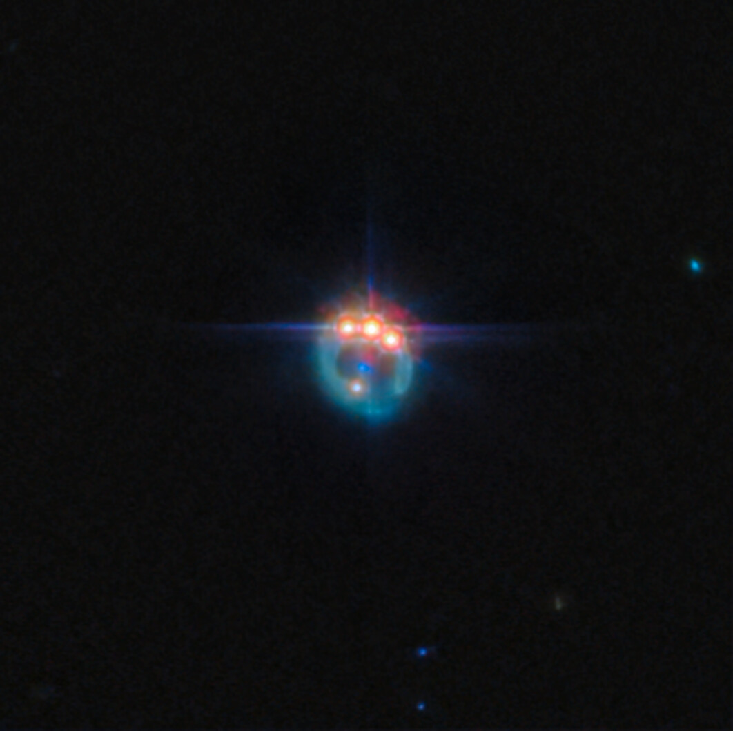 A bright, colorful object with blue, red, and orange lights appears against a dark space background, emitting star-like flares and a glowing halo&mdash;a scene reminiscent of a JWST reveal of the universe.
