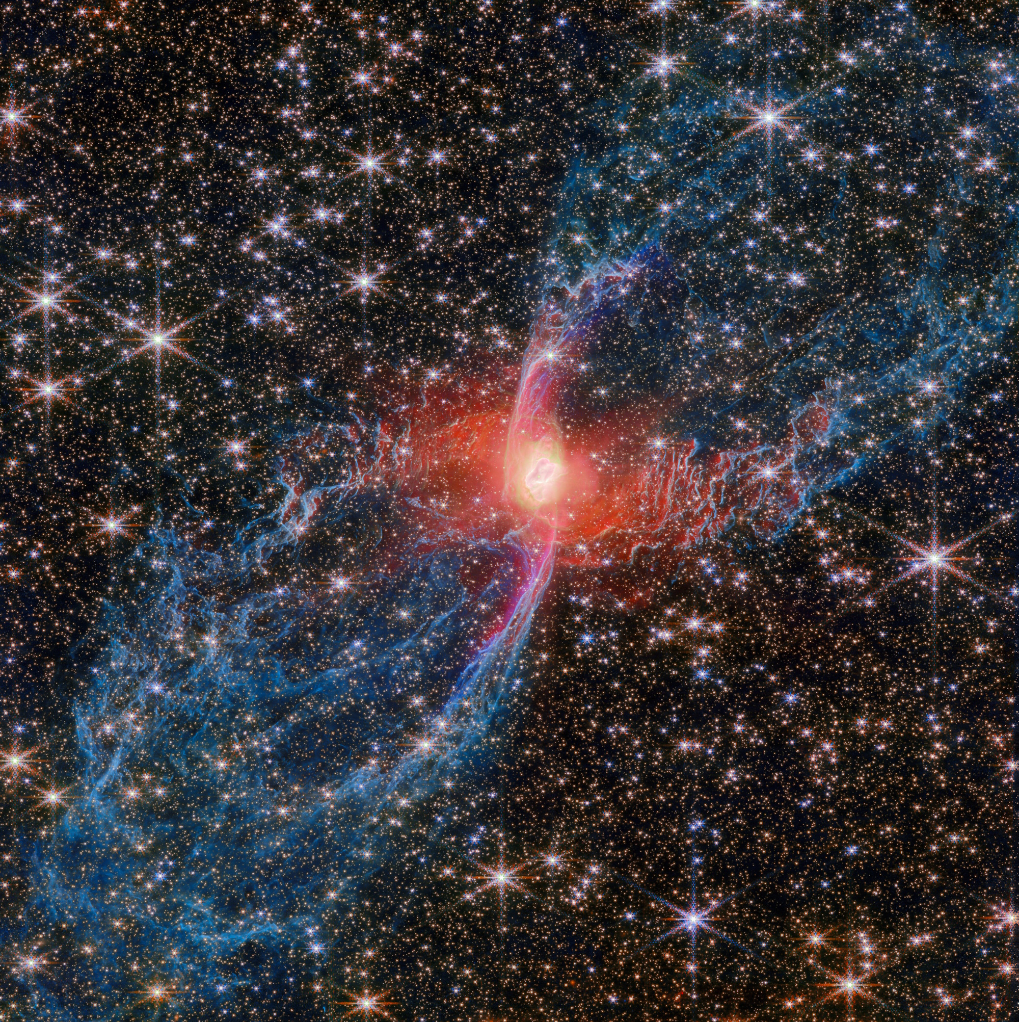 A bright, red-hued nebula with symmetrical blue filaments is surrounded by numerous stars in deep space, as JWST reveals the universe&rsquo;s hidden wonders.