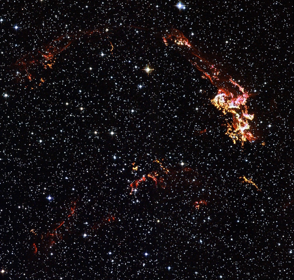 A star field with bright and colorful filaments of gas forming visible arcs, representing the remnants of Kepler's supernova as captured by NASA Chandra, set against a dark background.