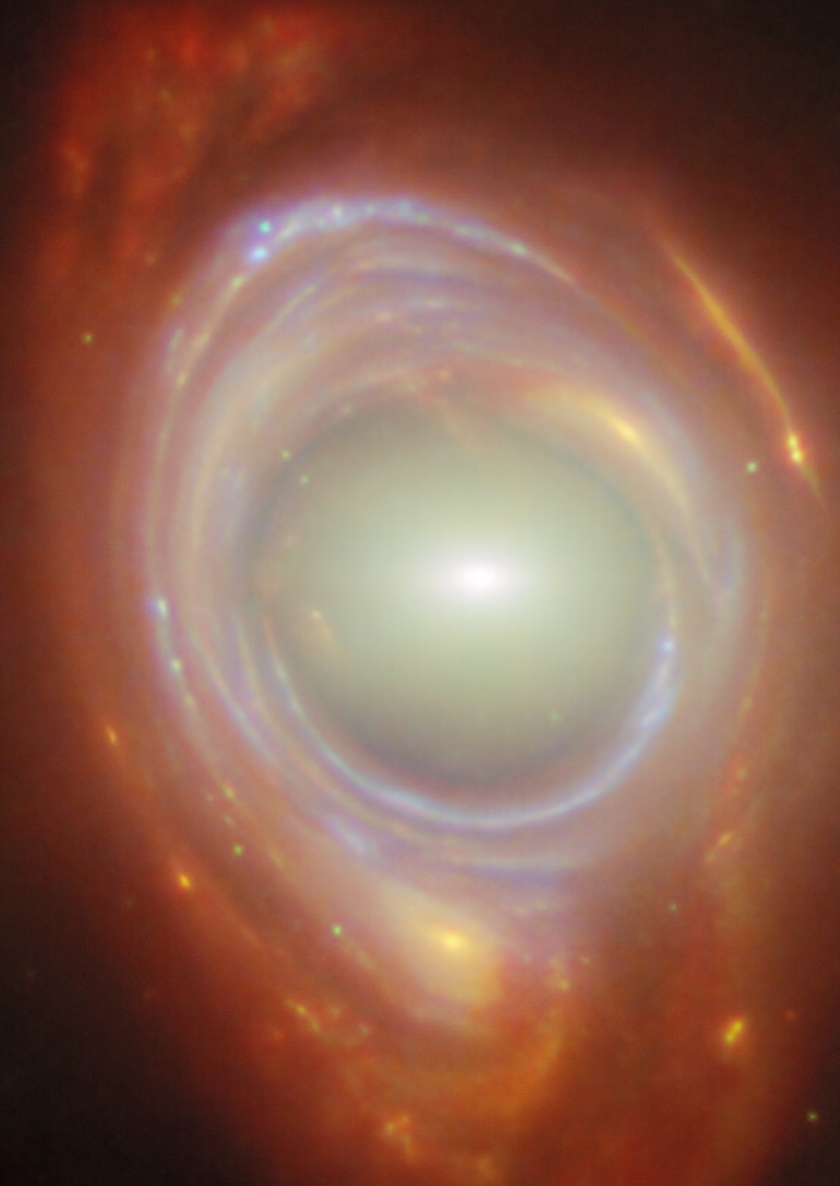 A close-up image of a galaxy with a bright core surrounded by glowing rings of gas and dust, in vibrant red, orange, and blue hues&mdash;an awe-inspiring scene that the JWST reveal brings to our universe.