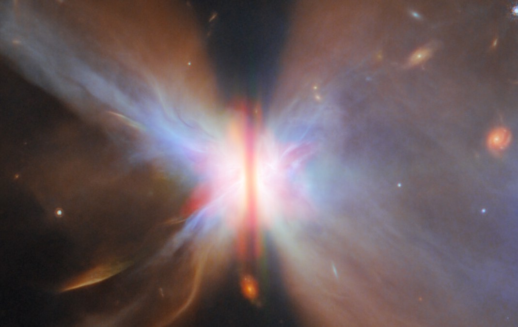 A colorful nebula with a bright center and symmetrical, wing-like clouds of gas and dust extends outward in space, as seen in a JWST reveal that uncovers stars and galaxies in the universe beyond.