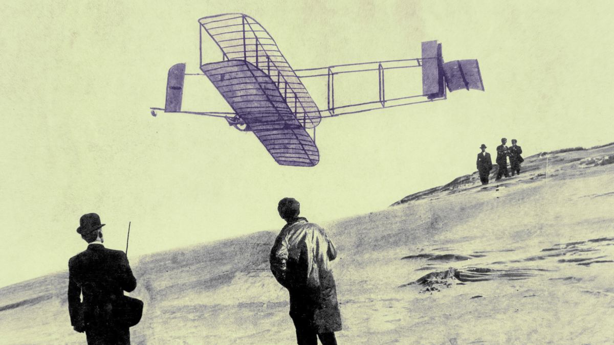 A vintage photograph shows a Wright Brothers-era biplane flying low over a sandy hill as four people on the ground watch.