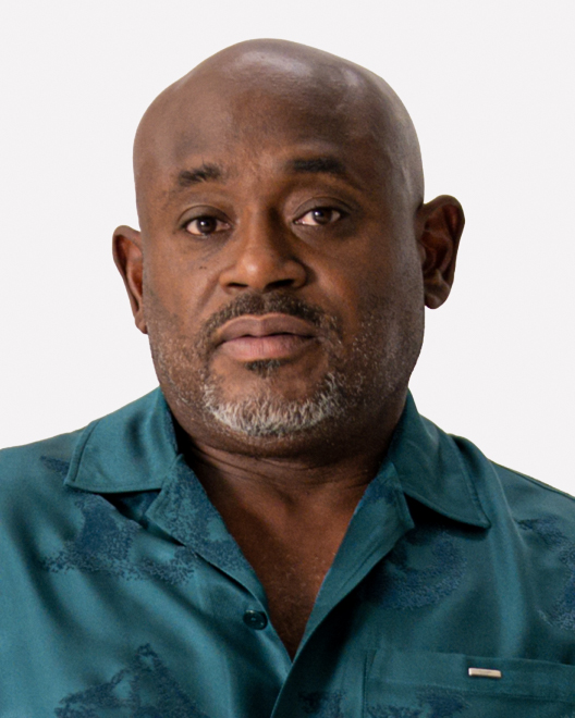 A middle-aged man with a bald head, trimmed gray beard, and teal button-up shirt looks directly at the camera against a plain background.