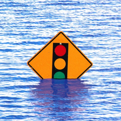 A traffic signal warning sign is partially submerged in floodwater.