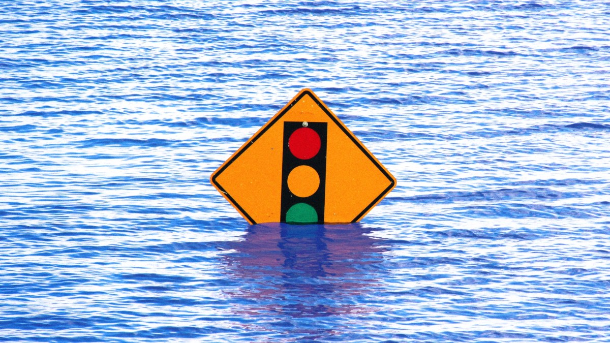 A traffic signal warning sign is partially submerged in floodwater.