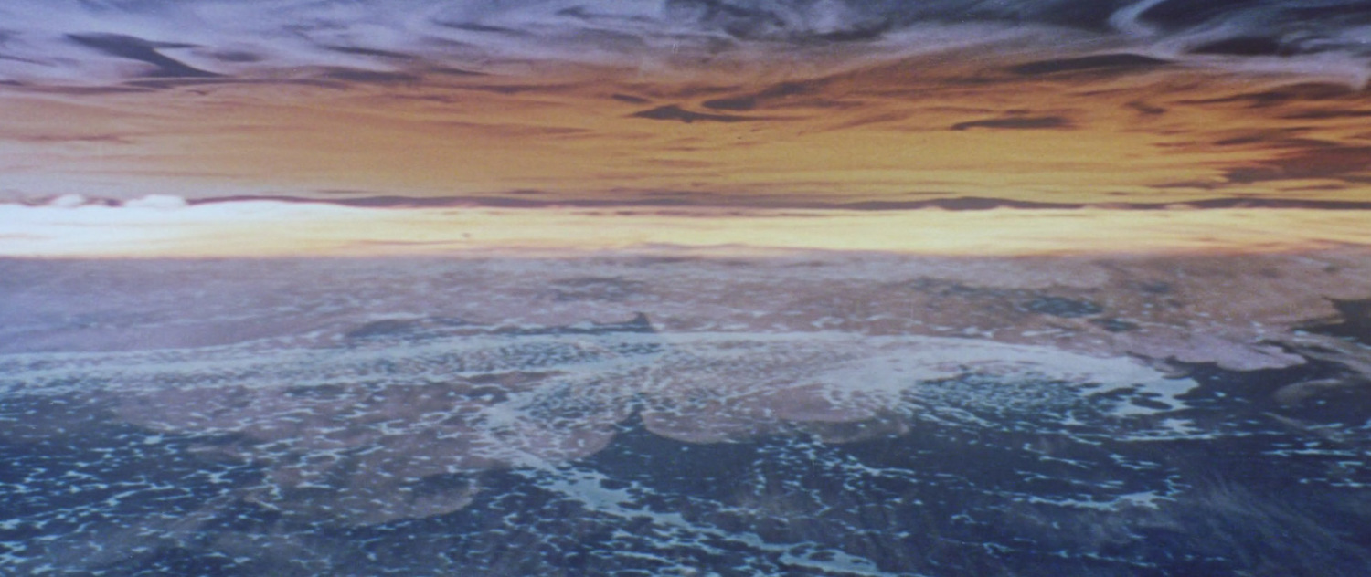 A view of Earth&rsquo;s surface with ice and water, beneath a dramatic yellow and orange cloud-covered sky, as if seen from above by curious aliens exploring our planet.