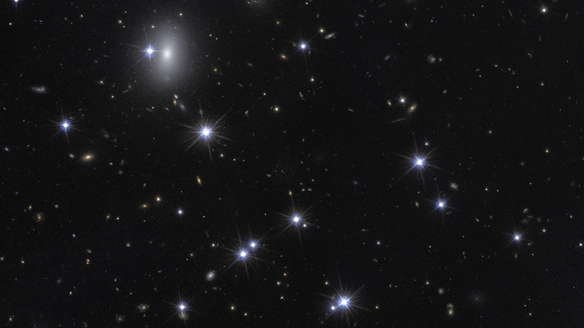 A view of a star-filled night sky with numerous bright stars and distant galaxies, including Hubble-dark galaxy formations, scattered across a dark background.