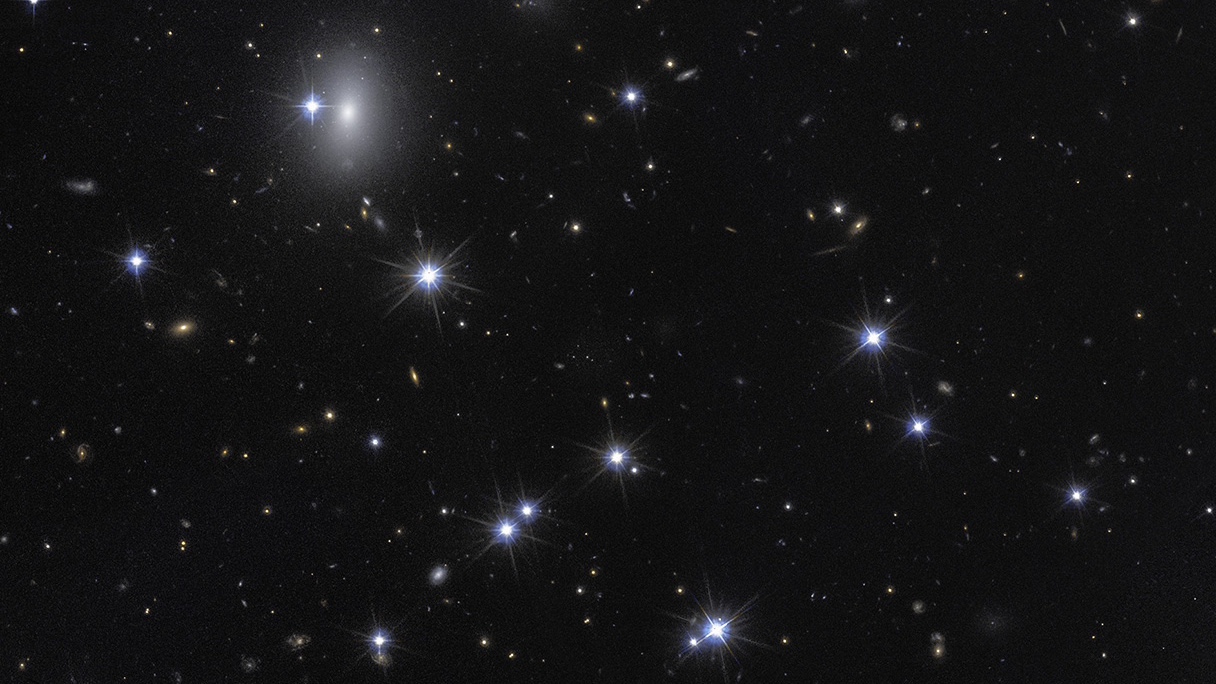 A view of a star-filled night sky with numerous bright stars and distant galaxies, including Hubble-dark galaxy formations, scattered across a dark background.